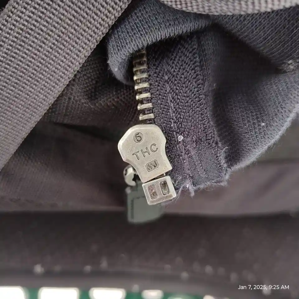 A close-up photo shows a silver zipper pull on dark gray fabric, with the letters 'THC' and the number '5' visibly stamped…