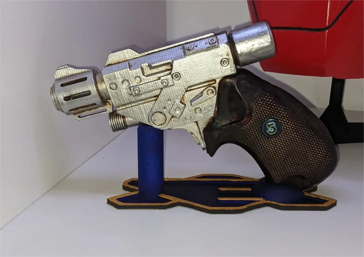 A 3D-printed replica of a sci-fi blaster pistol, featuring a metallic silver body with visible layer lines, a dark brown…
