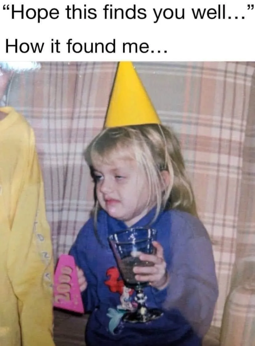 A young child with blonde hair wearing a yellow party hat and a blue shirt holds a glass goblet filled with a dark liquid…