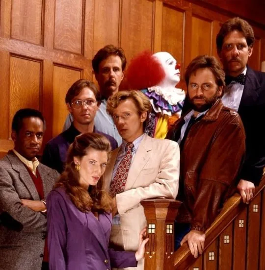 A promotional photo of the cast of 'The West Wing' is edited to include a red-haired clown with white face paint and ruffled…