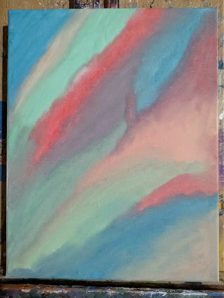 An abstract painting on canvas with diagonal streaks of blue, teal, red, and pink, resting on a paint-splattered wooden…