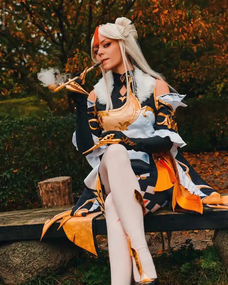 A cosplayer dressed as the character Diluc from Genshin Impact sits on a wooden bench outdoors, smoking a pipe and exhaling…