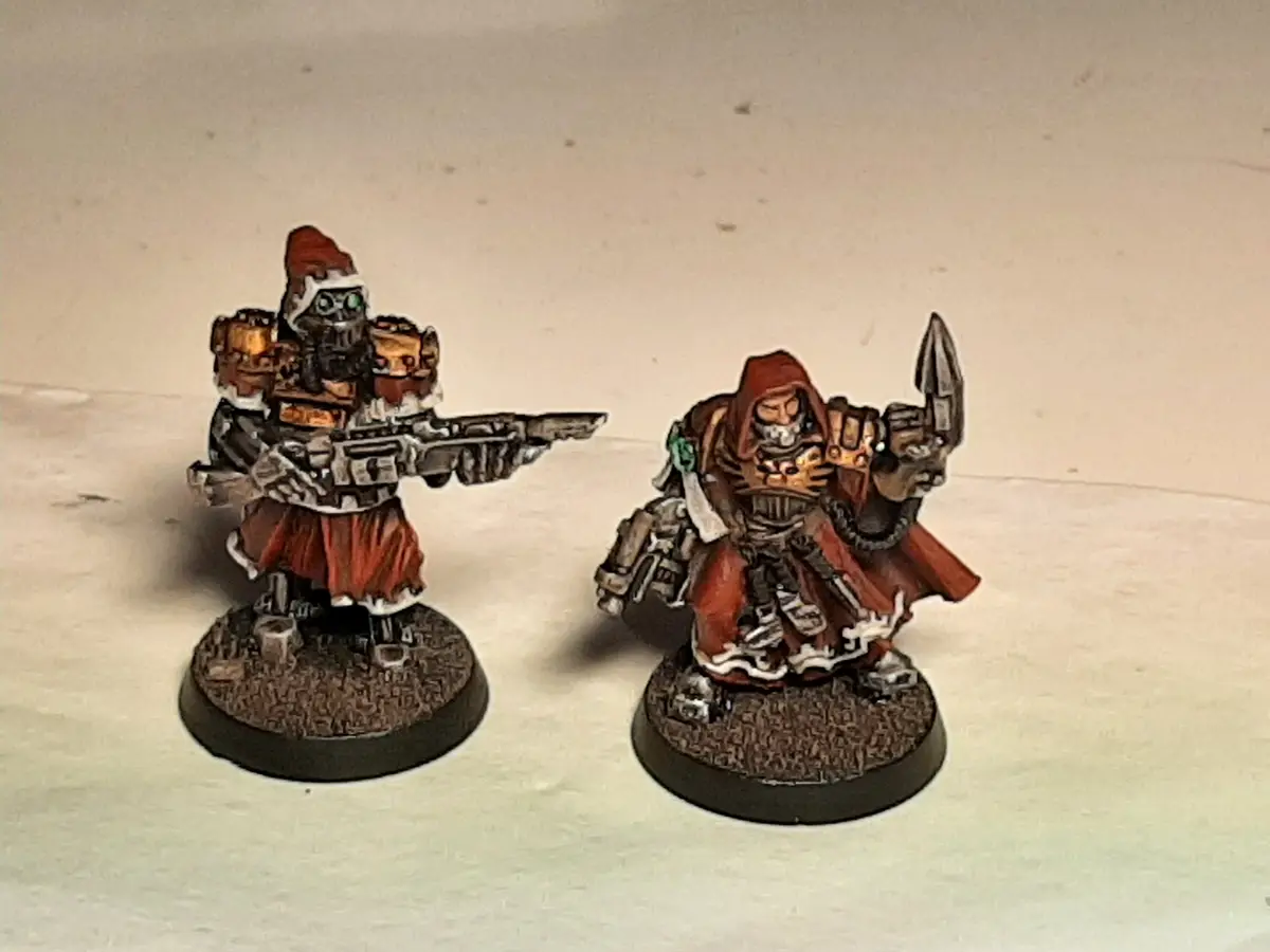 Two painted miniature figures, one wearing a Santa hat and holding a gun, the other in a red hooded cloak holding a spear…